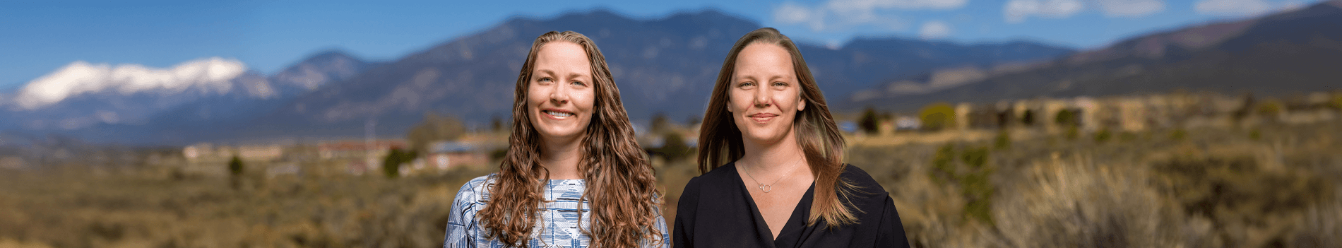Two women stand smiling outdoors against a backdrop of mountains, representing the Holy Cross Women's Health Institute.