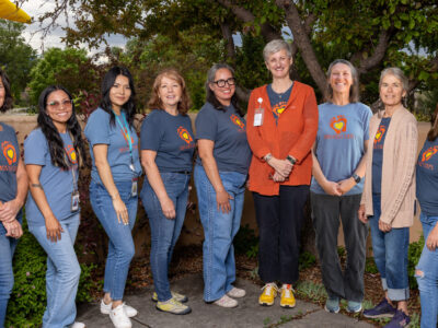 A group of diverse women smiling together, representing the First Steps program in a welcoming outdoor setting.