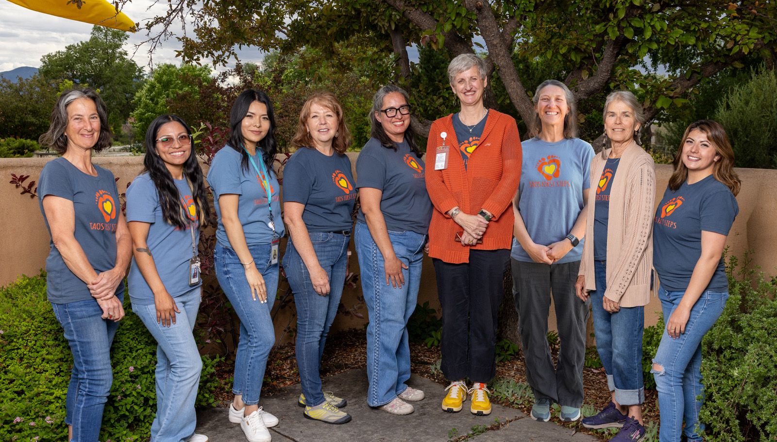 A group of diverse women smiling together, representing the First Steps program in a welcoming outdoor setting.