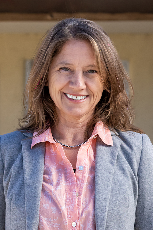 Jeannie Ross smiles confidently in a blazer and pink blouse, standing outdoors against a neutral background.