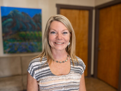 Smiling woman stands in a welcoming room, promoting community support for cancer patients at Taos Cancer Support Services.