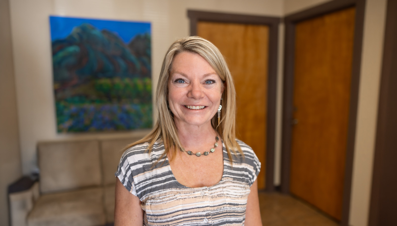 Smiling woman stands in a welcoming room, promoting community support for cancer patients at Taos Cancer Support Services.