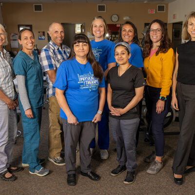 A diverse team of professionals stands together in a physical therapy clinic, representing Taos Physical Therapy.