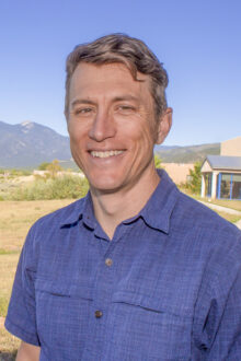 Doug Kast smiles confidently outdoors, with mountains and greenery in the background, showcasing a professional demeanor.