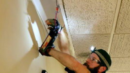 An electrician installs energy-efficient lighting while using a ladder, highlighting the Trane Energy Saving Project.