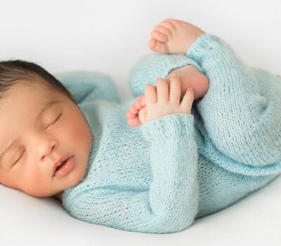 Newborn baby in a light blue outfit, peacefully sleeping on a soft, white background.