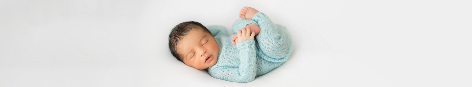 Newborn baby in a light blue outfit, peacefully sleeping on a soft, white background.