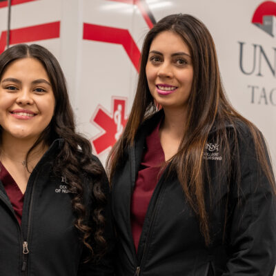 Two nursing students smile confidently in front of a UNM-Taos ambulance, highlighting career opportunities in healthcare.