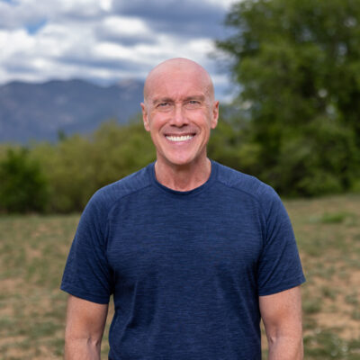 Smiling man in a blue shirt stands outdoors with mountains in the background, promoting orthopedic foot and ankle surgery.