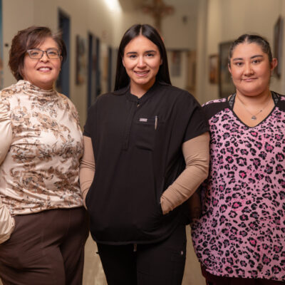 Three women, dressed in medical attire, stand together in a hallway, showcasing community and support in health care careers.