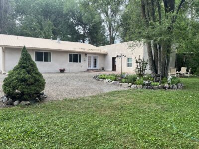 A cozy, landscaped home featuring a gravel driveway, greenery, and outdoor seating in a serene setting.