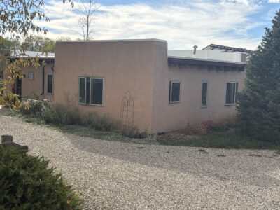 Stucco building with large windows, surrounded by gravel and greenery, under a partly cloudy sky.